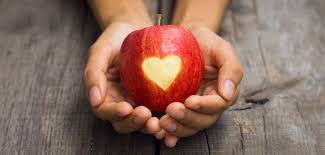 hands holding a red apple with a shape of a heart cut out of skin